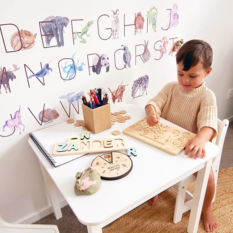 animal letters wall stickers on a wall behind a little child doing a puzzle